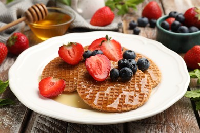 Photo of Tasty Dutch waffles (stroopwafels) with honey, strawberries and blueberries on wooden table, closeup