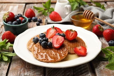 Photo of Tasty Dutch waffles (stroopwafels) with honey, berries and mint on wooden table, closeup