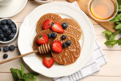 Photo of Tasty Dutch waffles (stroopwafels) with honey, berries and mint on light wooden table, flat lay