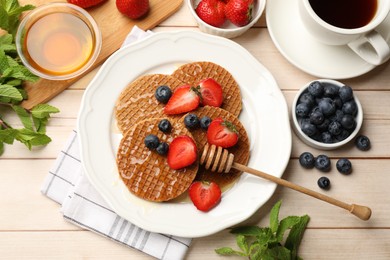 Photo of Tasty Dutch waffles (stroopwafels) with honey, berries and mint on light wooden table, flat lay
