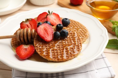 Photo of Tasty Dutch waffles (stroopwafels) with honey, strawberries and blueberries on light wooden table, closeup