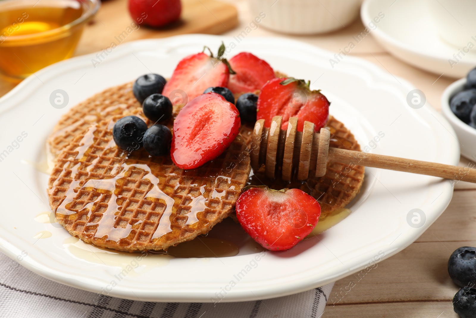 Tasty Dutch waffles (stroopwafels) with honey, strawberries and blueberries on light wooden table, closeup Photo of Tasty Dutch waffles (stroopwafels) with honey, strawberries and blueberries on light wooden table, closeup