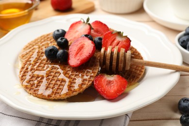 Photo of Tasty Dutch waffles (stroopwafels) with honey, strawberries and blueberries on light wooden table, closeup