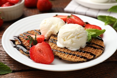 Photo of Tasty Dutch waffles (stroopwafels) with strawberries, ice cream and chocolate sauce on wooden table, closeup