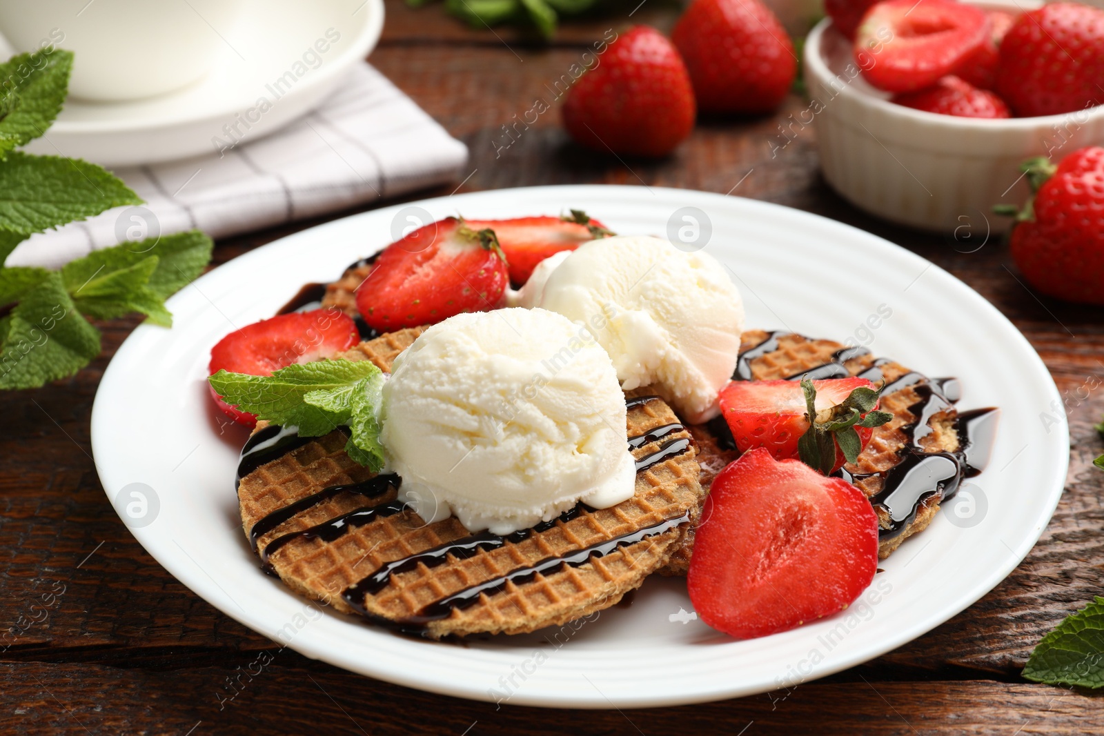 Tasty Dutch waffles (stroopwafels) with strawberries, ice cream and chocolate sauce on wooden table, closeup Photo of Tasty Dutch waffles (stroopwafels) with strawberries, ice cream and chocolate sauce on wooden table, closeup