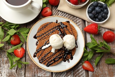 Photo of Tasty Dutch waffles (stroopwafels) with ice cream, chocolate sauce, mint and strawberries on wooden table, flat lay