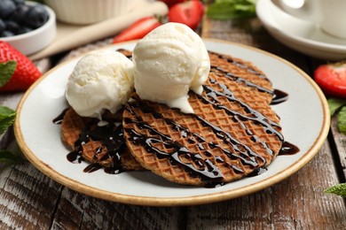 Photo of Tasty Dutch waffles (stroopwafels) with ice cream and chocolate sauce on wooden table, closeup