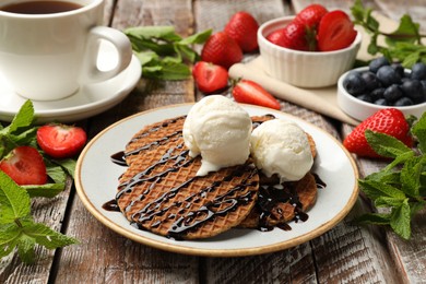 Photo of Tasty Dutch waffles (stroopwafels) with ice cream, chocolate sauce, mint and strawberries on wooden table, closeup
