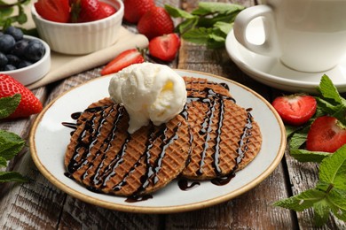 Photo of Tasty Dutch waffles (stroopwafels) with ice cream, chocolate sauce, mint and strawberries on wooden table, closeup