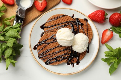 Photo of Tasty Dutch waffles (stroopwafels) with ice cream, chocolate sauce, mint and strawberries on white table, flat lay