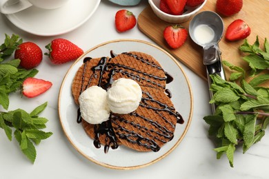 Photo of Tasty Dutch waffles (stroopwafels) with ice cream, chocolate sauce, mint and strawberries on white table, flat lay