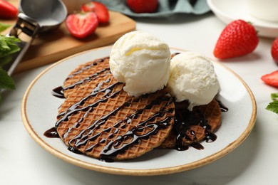 Photo of Tasty Dutch waffles (stroopwafels) with ice cream and chocolate sauce on white table, closeup