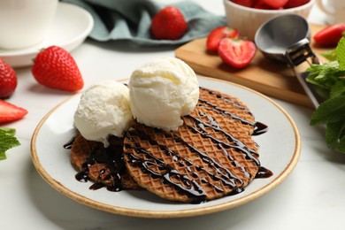 Photo of Tasty Dutch waffles (stroopwafels) with ice cream and chocolate sauce on white table, closeup