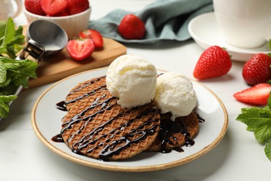 Photo of Tasty Dutch waffles (stroopwafels) with ice cream and chocolate sauce on white table, closeup