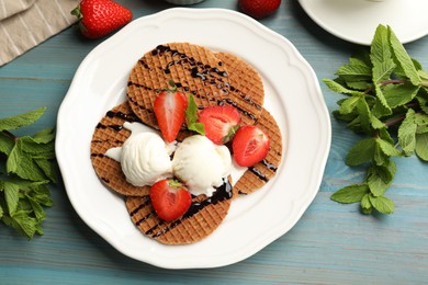 Photo of Tasty Dutch waffles (stroopwafels) with ice cream, chocolate sauce, mint and strawberries on light blue wooden table, flat lay