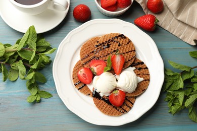 Photo of Tasty Dutch waffles (stroopwafels) with ice cream, chocolate sauce, mint and strawberries on light blue wooden table, flat lay