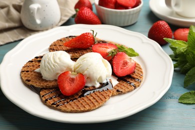 Photo of Tasty Dutch waffles (stroopwafels) with ice cream, chocolate sauce, mint and strawberries on light blue wooden table, closeup