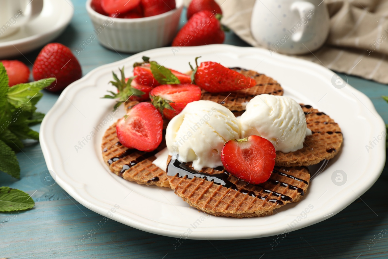 Tasty Dutch waffles (stroopwafels) with ice cream, chocolate sauce, mint and strawberries on light blue wooden table, closeup Photo of Tasty Dutch waffles (stroopwafels) with ice cream, chocolate sauce, mint and strawberries on light blue wooden table, closeup