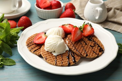 Photo of Tasty Dutch waffles (stroopwafels) with ice cream, chocolate sauce, mint and strawberries on light blue wooden table, closeup
