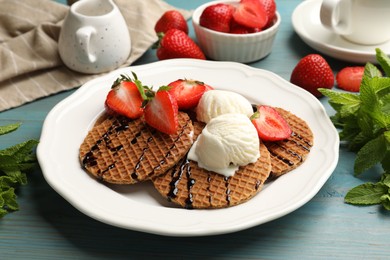Photo of Tasty Dutch waffles (stroopwafels) with ice cream, chocolate sauce, mint and strawberries on light blue wooden table, closeup