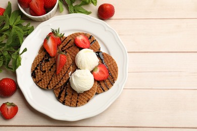 Photo of Tasty Dutch waffles (stroopwafels) with ice cream, chocolate sauce, mint and strawberries on light wooden table, flat lay. Space for text