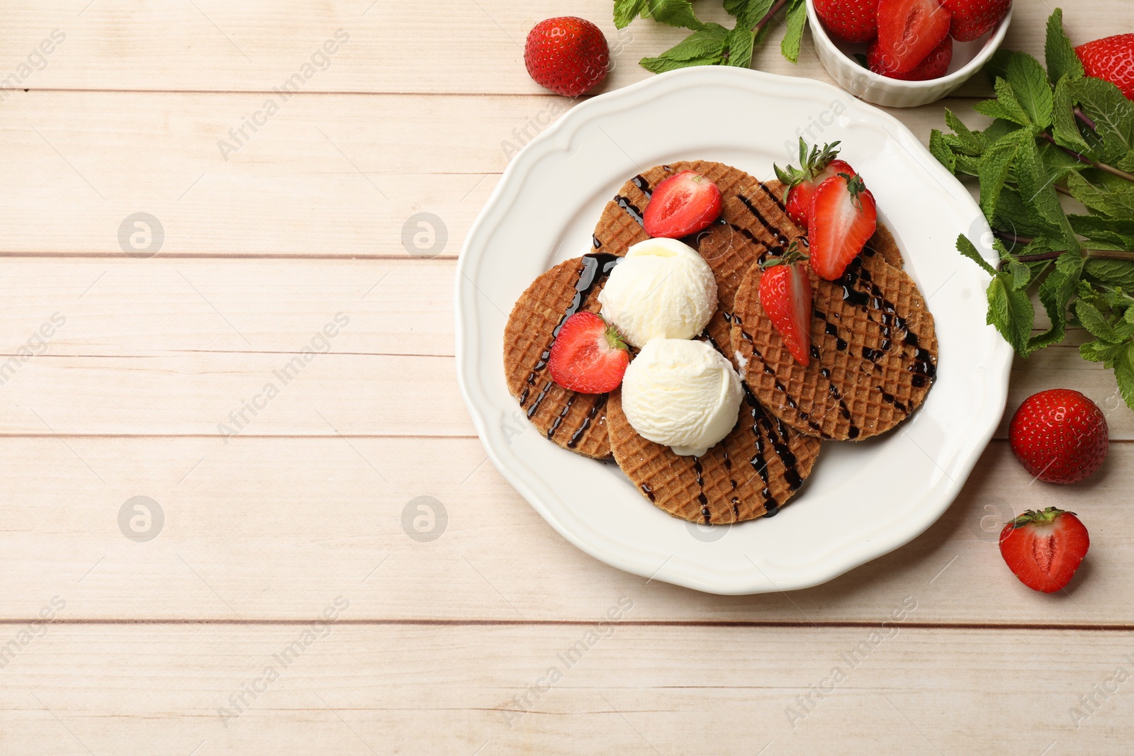 Tasty Dutch waffles (stroopwafels) with ice cream, chocolate sauce, mint and strawberries on light wooden table, flat lay. Space for text Photo of Tasty Dutch waffles (stroopwafels) with ice cream, chocolate sauce, mint and strawberries on light wooden table, flat lay. Space for text