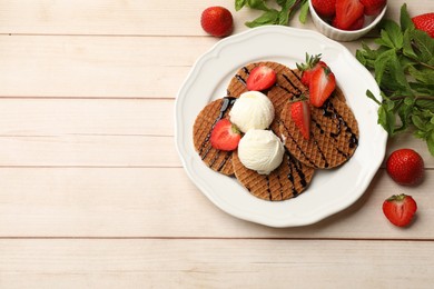 Photo of Tasty Dutch waffles (stroopwafels) with ice cream, chocolate sauce, mint and strawberries on light wooden table, flat lay. Space for text
