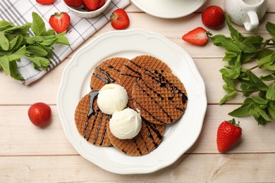 Photo of Tasty Dutch waffles (stroopwafels) with ice cream, chocolate sauce, mint and strawberries on light wooden table, flat lay