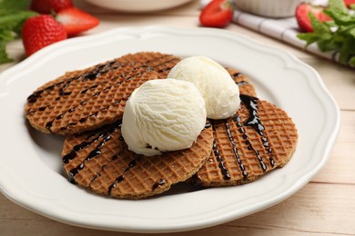 Photo of Tasty Dutch waffles (stroopwafels) with ice cream and chocolate sauce on light wooden table, closeup