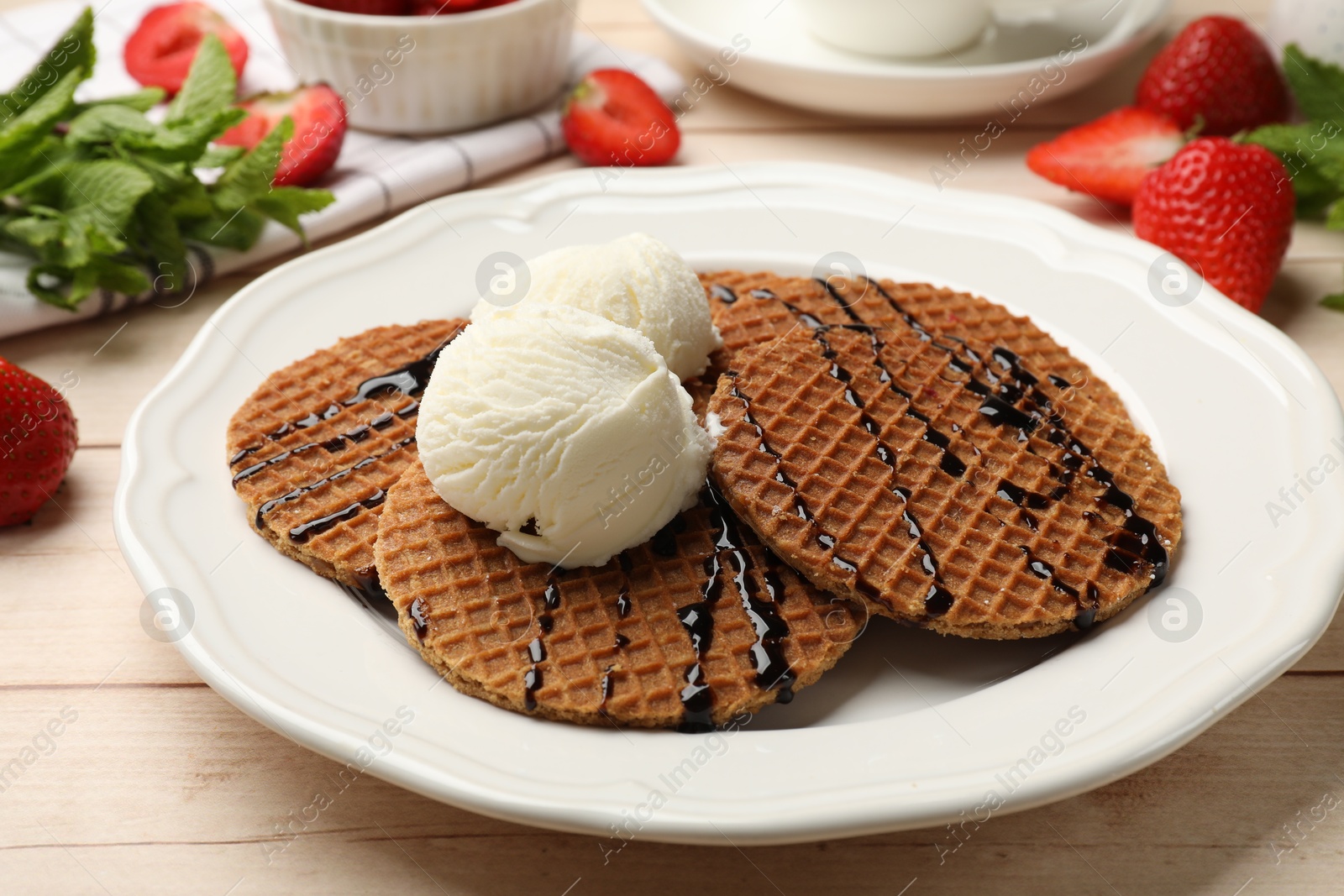 Tasty Dutch waffles (stroopwafels) with ice cream and chocolate sauce on light wooden table, closeup Photo of Tasty Dutch waffles (stroopwafels) with ice cream and chocolate sauce on light wooden table, closeup