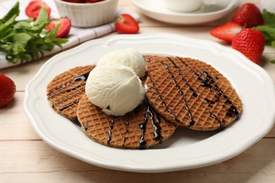 Photo of Tasty Dutch waffles (stroopwafels) with ice cream and chocolate sauce on light wooden table, closeup