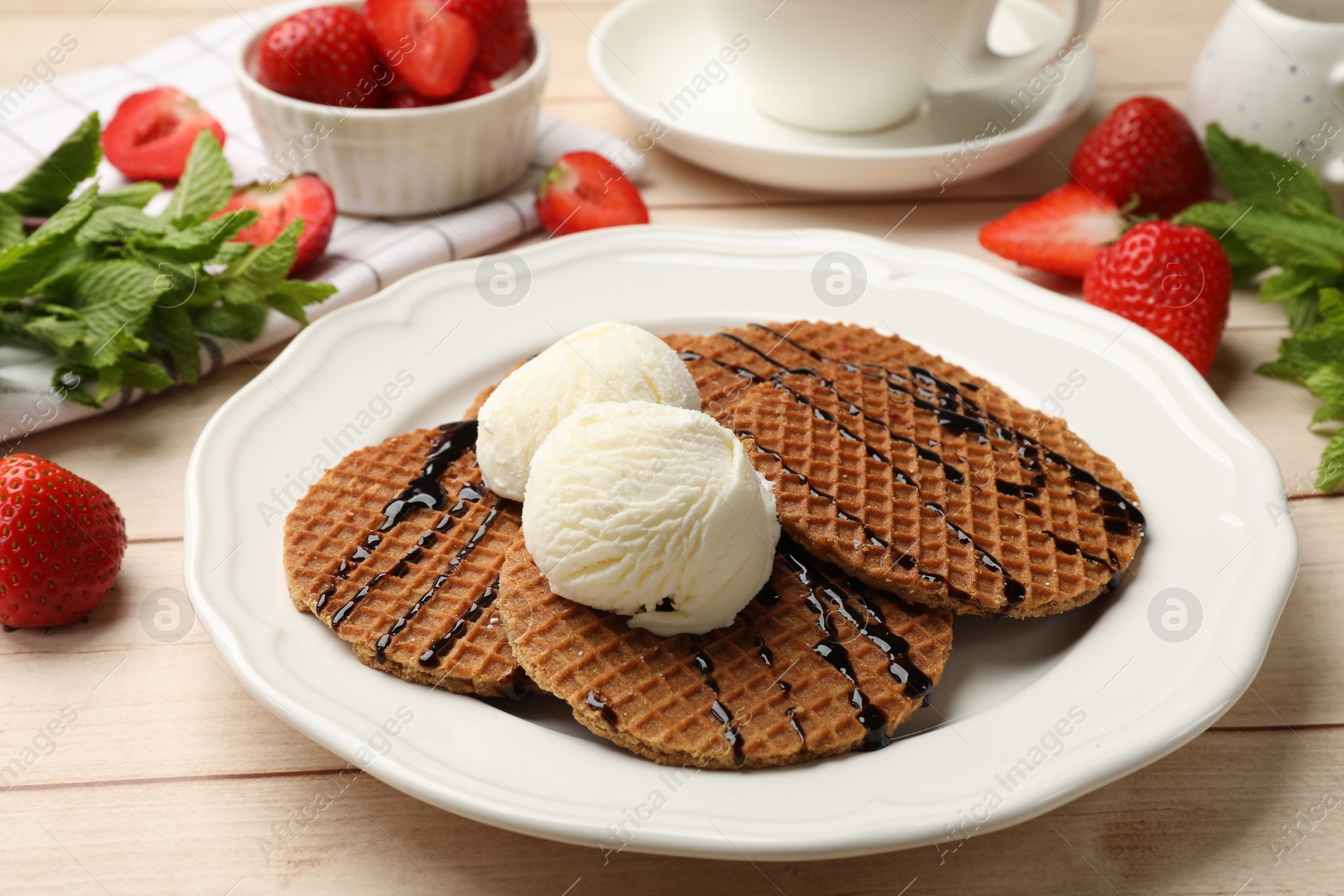 Tasty Dutch waffles (stroopwafels) with ice cream and chocolate sauce on light wooden table, closeup Photo of Tasty Dutch waffles (stroopwafels) with ice cream and chocolate sauce on light wooden table, closeup