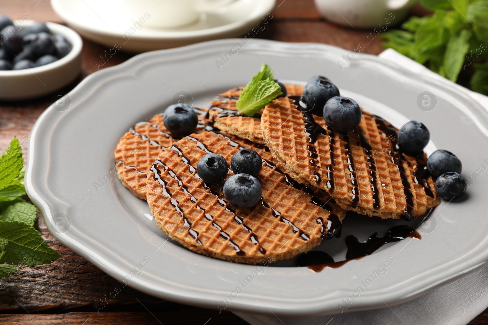 Tasty Dutch waffles (stroopwafels) with blueberries, mint and chocolate sauce on wooden table, closeup Photo of Tasty Dutch waffles (stroopwafels) with blueberries, mint and chocolate sauce on wooden table, closeup