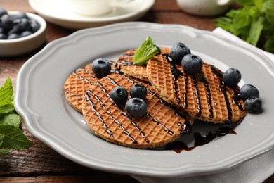 Photo of Tasty Dutch waffles (stroopwafels) with blueberries, mint and chocolate sauce on wooden table, closeup
