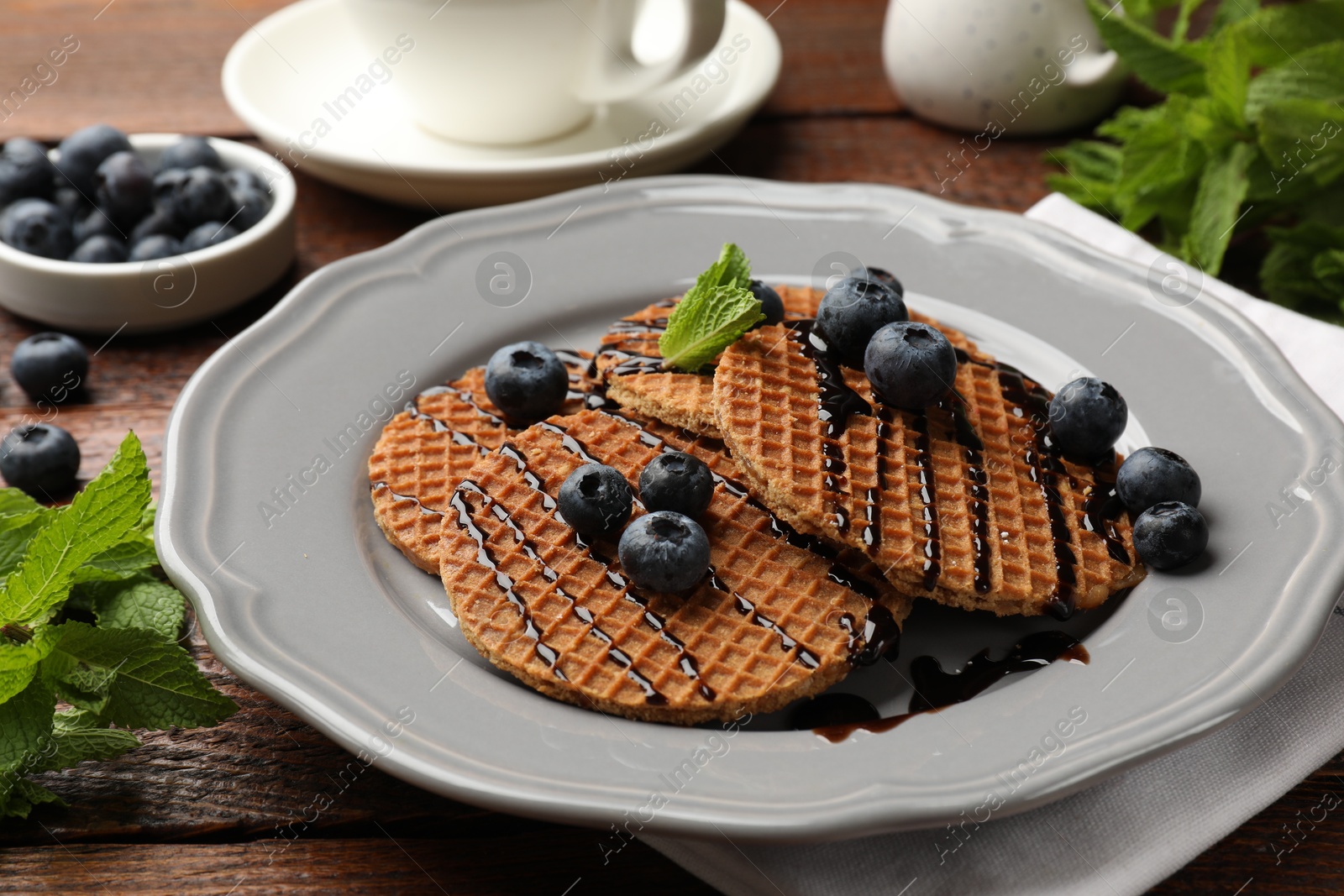 Tasty Dutch waffles (stroopwafels) with blueberries, mint and chocolate sauce on wooden table, closeup Photo of Tasty Dutch waffles (stroopwafels) with blueberries, mint and chocolate sauce on wooden table, closeup