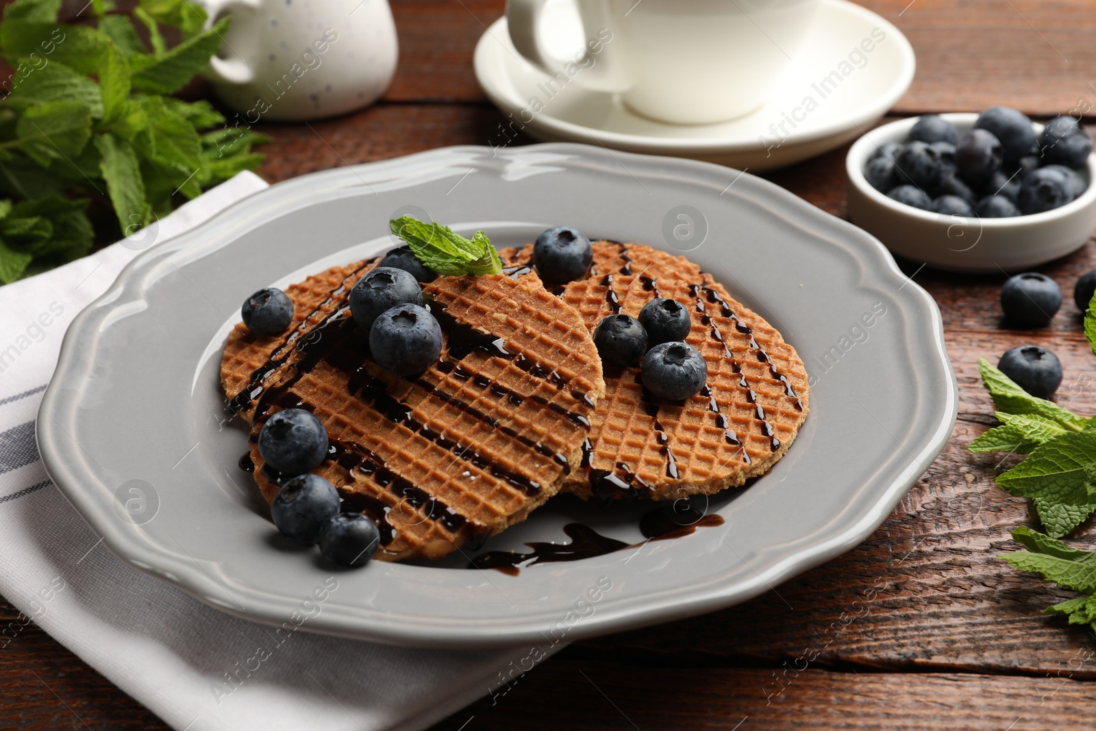 Tasty Dutch waffles (stroopwafels) with blueberries, mint and chocolate sauce on wooden table, closeup Photo of Tasty Dutch waffles (stroopwafels) with blueberries, mint and chocolate sauce on wooden table, closeup