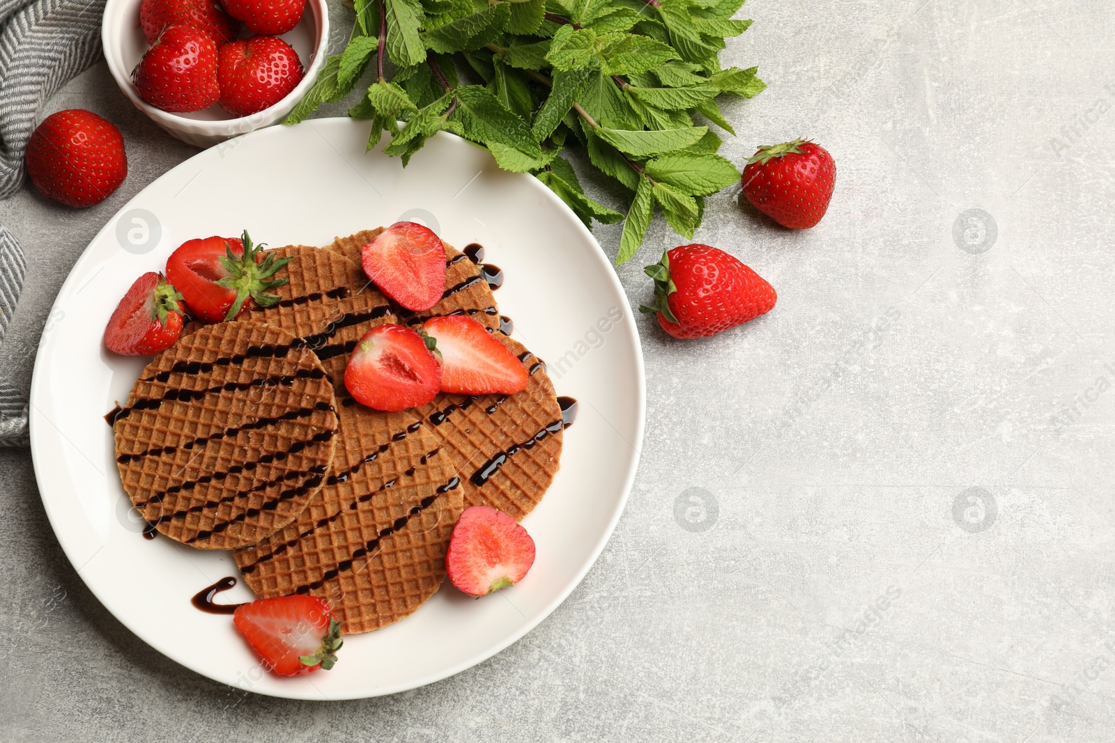 Tasty Dutch waffles (stroopwafels) with strawberries, mint and chocolate sauce on grey textured table, flat lay. Space for text Photo of Tasty Dutch waffles (stroopwafels) with strawberries, mint and chocolate sauce on grey textured table, flat lay. Space for text
