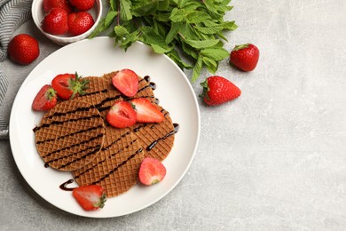 Photo of Tasty Dutch waffles (stroopwafels) with strawberries, mint and chocolate sauce on grey textured table, flat lay. Space for text