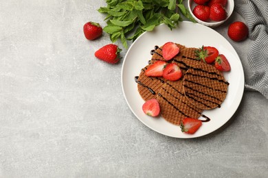 Photo of Tasty Dutch waffles (stroopwafels) with strawberries, mint and chocolate sauce on grey textured table, flat lay. Space for text