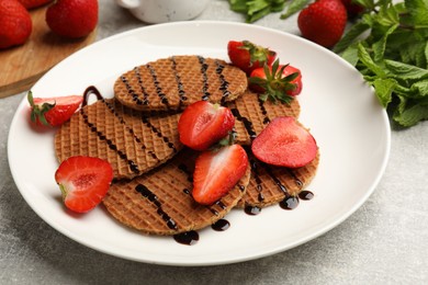 Photo of Tasty Dutch waffles (stroopwafels) with strawberries and chocolate sauce on grey textured table, closeup