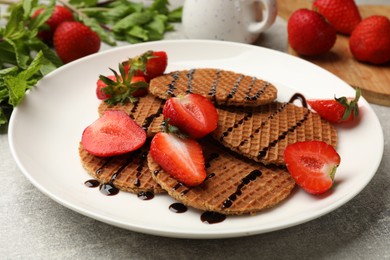 Photo of Tasty Dutch waffles (stroopwafels) with strawberries and chocolate sauce on grey textured table, closeup
