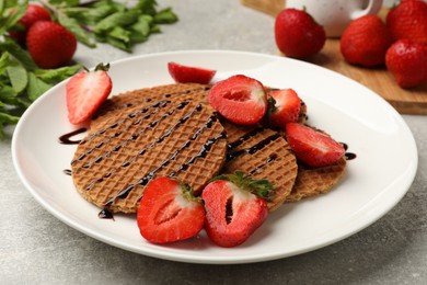 Photo of Tasty Dutch waffles (stroopwafels) with strawberries and chocolate sauce on grey textured table, closeup