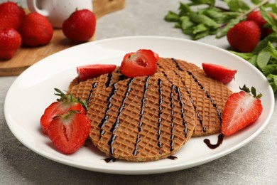 Photo of Tasty Dutch waffles (stroopwafels) with strawberries and chocolate sauce on grey textured table, closeup