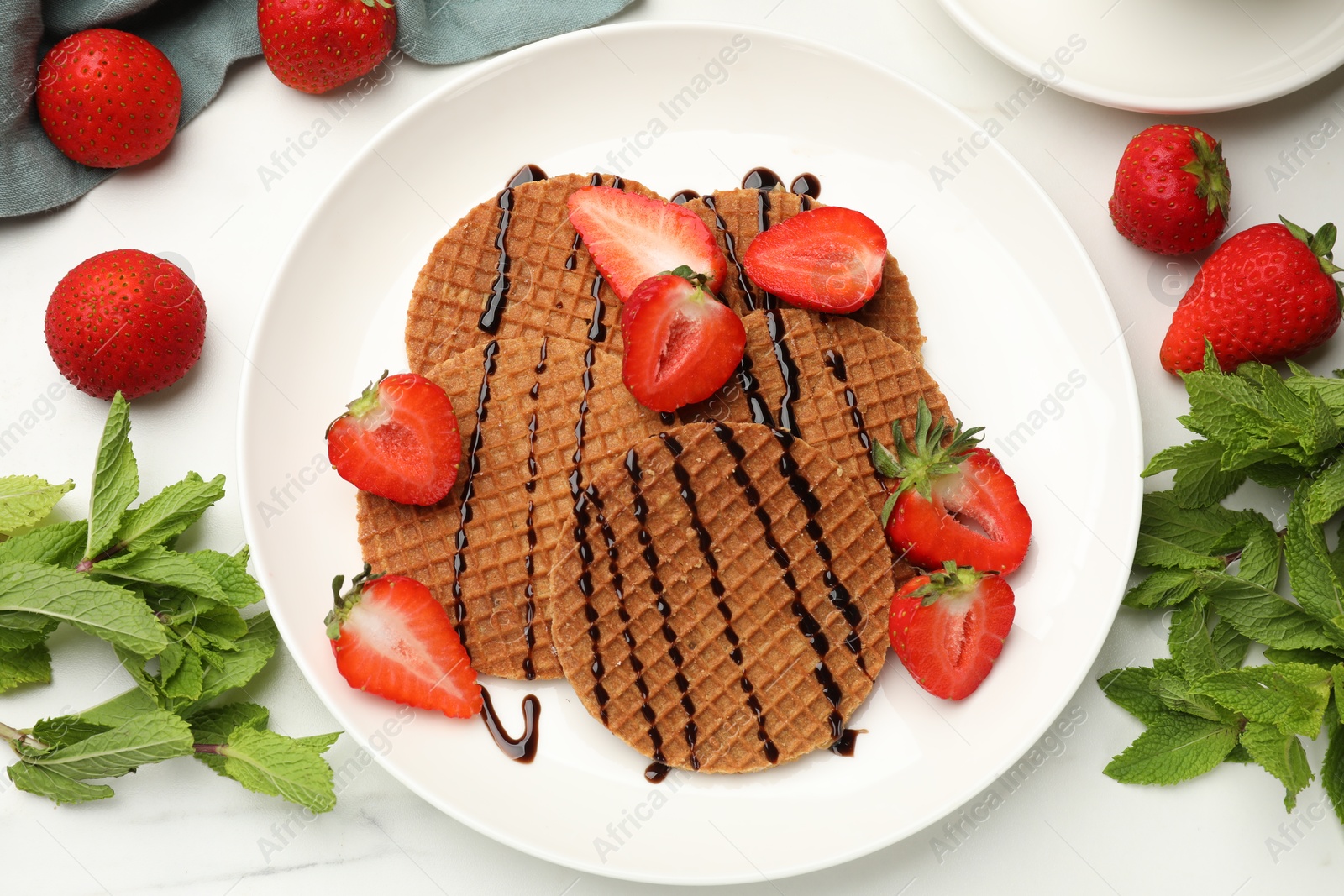 Tasty Dutch waffles (stroopwafels) with strawberries, mint and chocolate sauce on white marble table, flat lay Photo of Tasty Dutch waffles (stroopwafels) with strawberries, mint and chocolate sauce on white marble table, flat lay