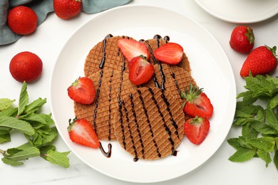 Photo of Tasty Dutch waffles (stroopwafels) with strawberries, mint and chocolate sauce on white marble table, flat lay