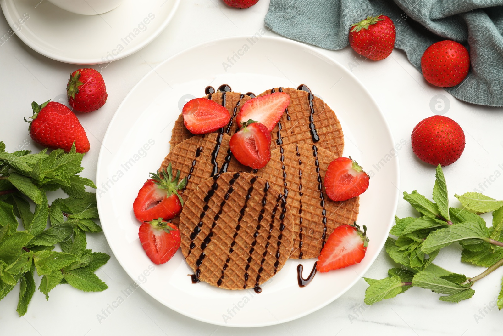 Tasty Dutch waffles (stroopwafels) with strawberries, mint and chocolate sauce on white marble table, flat lay Photo of Tasty Dutch waffles (stroopwafels) with strawberries, mint and chocolate sauce on white marble table, flat lay
