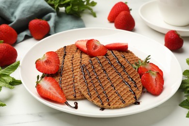 Photo of Tasty Dutch waffles (stroopwafels) with strawberries, mint and chocolate sauce on white marble table, closeup