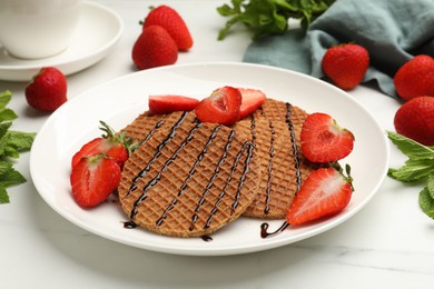 Photo of Tasty Dutch waffles (stroopwafels) with strawberries, mint and chocolate sauce on white marble table, closeup