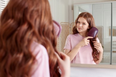 Photo of Teenage girl brushing her shiny hair near mirror at home