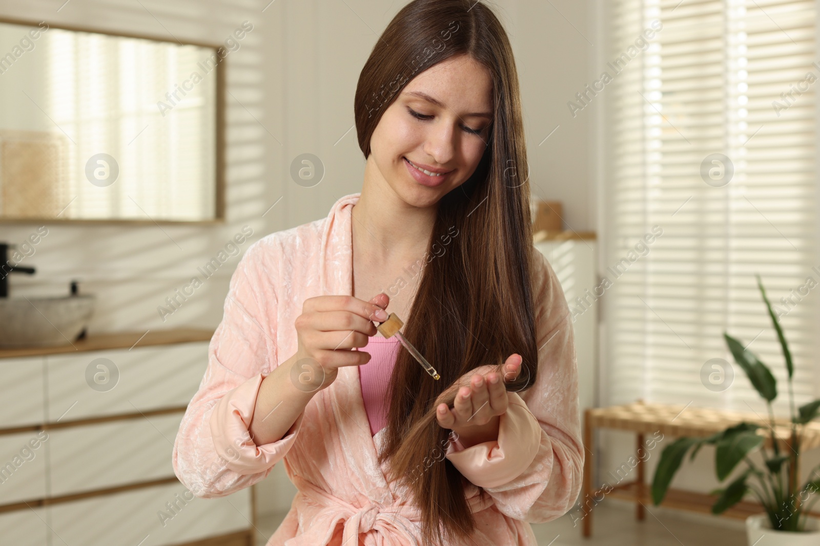 Smiling teenage girl applying serum onto her hair at home Photo of Smiling teenage girl applying serum onto her hair at home